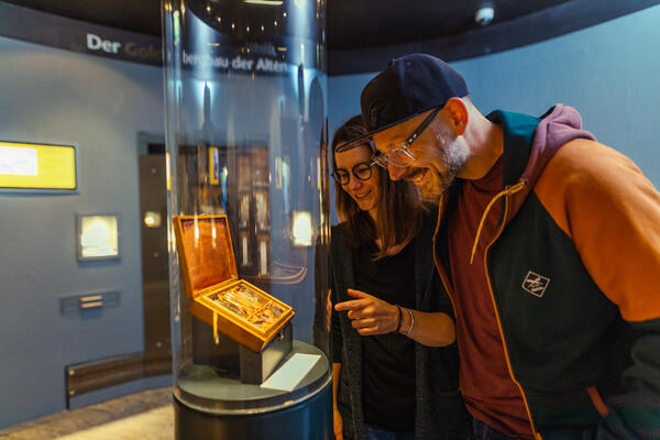 Bild vergrößern: Ein Mann und eine Frau betrachten im Gewölbekeller des Korbacher Museums das Goldkästchen mit Goldproben aus dem Eisenberg.