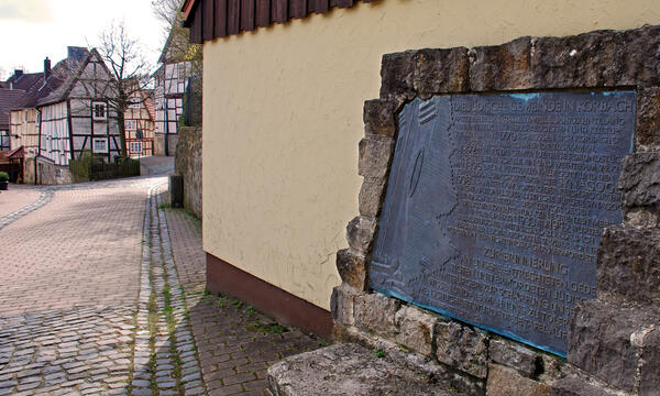 Bild vergrößern: Der Gedenkstein an die in der Pogromnacht zerstörte Korbcher Synagoge, eine von Bruchsteinen eingefasste Bronzeplatte mit Inschrift.